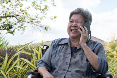 Smiling woman using mobile phone while sitting on wheelchair