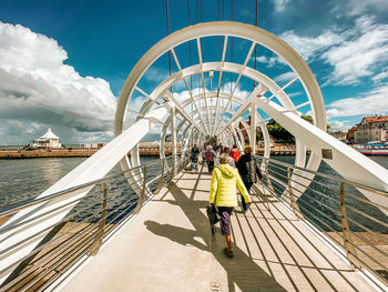 Rear view of women with umbrella on bridge against sky