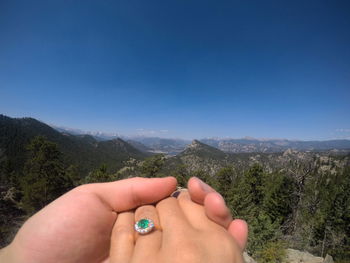 Midsection of person hand against mountain against clear blue sky