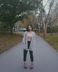 Portrait of young woman standing on road against trees