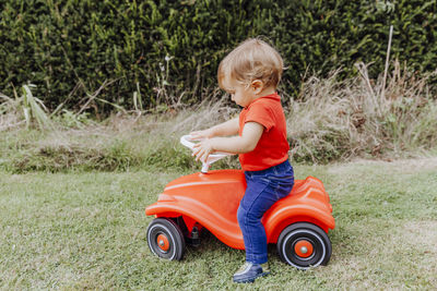 Side view of baby girl riding toy car on grassy field