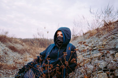 Man wearing hood while sitting on field