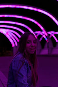 Portrait of smiling young woman against illuminated purple lighting