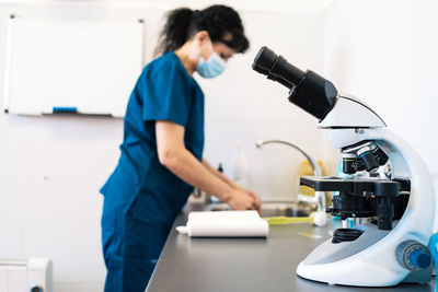 Modern microscope placed on table near female doctor in medical mask in lab of modern clinic