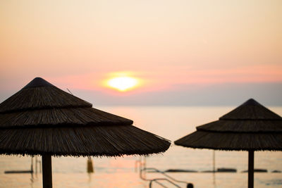 Thatched parasols at beach against sky during sunset