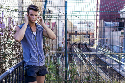 Portrait of man listening music standing by fence