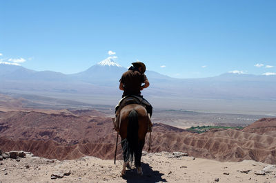 Rear view of man riding horse at desert against volcano
