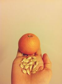 Close-up of hand holding apple against orange background