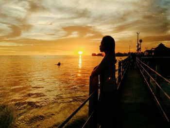 Rear view of silhouette woman standing on sea against sky during sunset