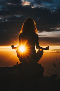 Silhouette woman sitting by sea against sky during sunset