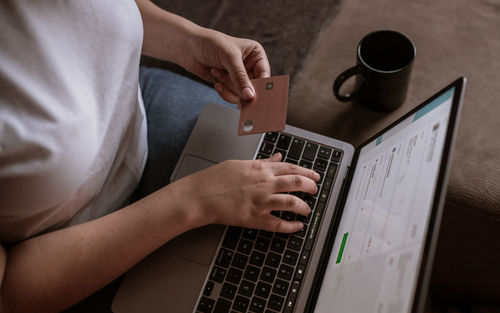 Young woman using laptop and card for financial services on the couch