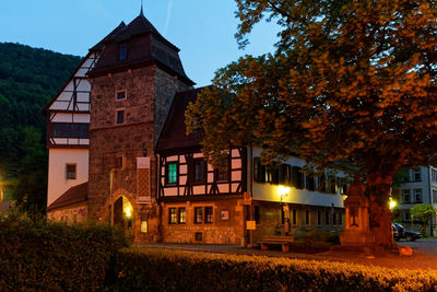 House by illuminated building against sky at dusk