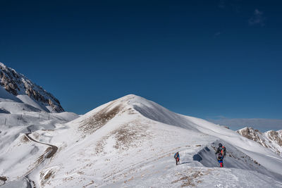 People climbing on snowcapped mountain against clear sky