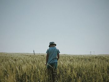 Rear view of man standing in wheat field against clear sky