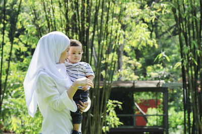 Happy mother and daughter on plant against trees