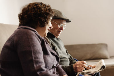 Senior couple reading newspaper while sitting on sofa at home