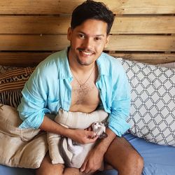 Portrait of smiling man holding cat while sitting on bed at home