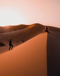 Couple sitting in the sahara desert in morocco during sunset