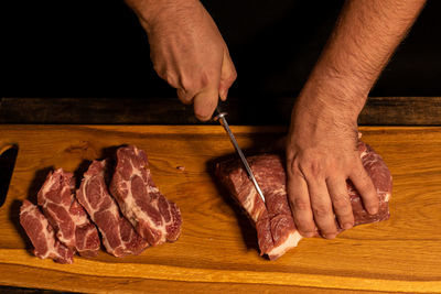 Close-up of male hands slicing meat.