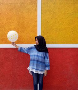 Woman holding balloon while standing against wall