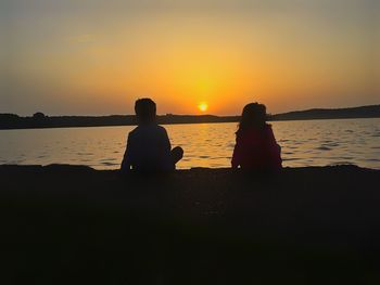 Silhouette people sitting on beach against sky during sunset