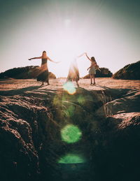 People standing on rocks by land against sky