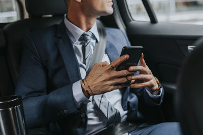 Midsection of businessman holding smart phone while sitting in car