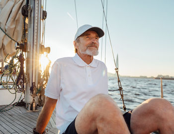 Rear view of man sitting by sea against sky