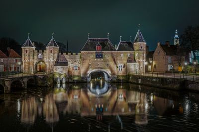 Arch bridge over river by buildings against sky at night