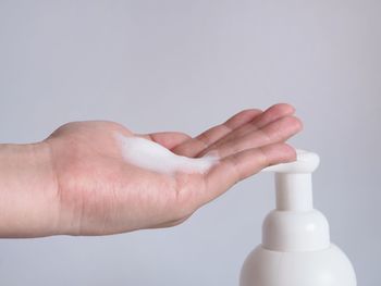 Close-up of hand holding bottle against white background