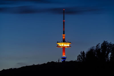 Illuminated lighthouse by building against sky at dusk