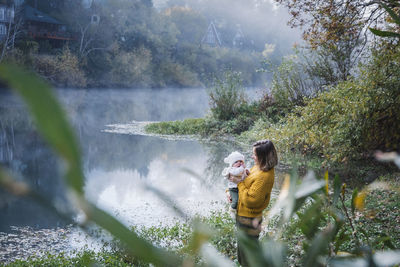 A woman is holding a baby near a river