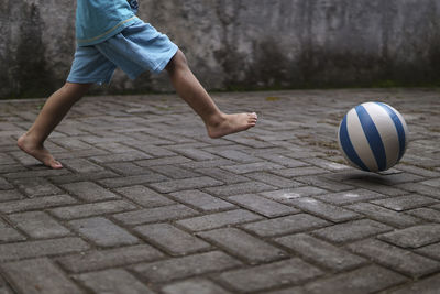 Low section of child playing with ball on footpath