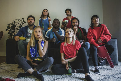 Male and female fans watching soccer match while sitting at home