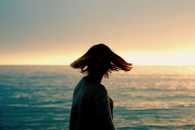 Young woman by sea against sky during sunset