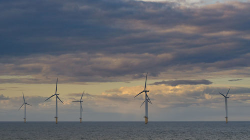 Windmills on sea against sky during sunset