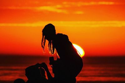 Silhouette woman on beach against orange sky