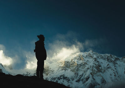 Silhouette man standing on snowcapped mountain against sky
