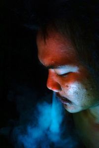 Close-up portrait of man smoking against black background