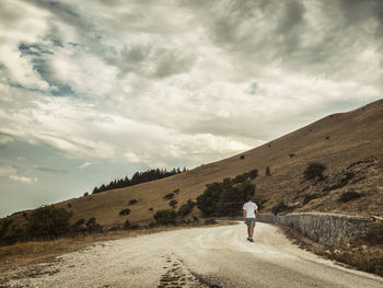 Rear view of man walking on road against sky