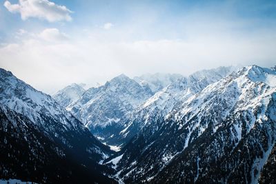 Scenic view of snowcapped mountains against cloudy sky on sunny day