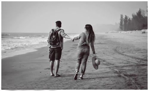 Rear view of couple holding hands at beach