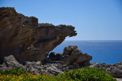 Rock formation by sea against clear blue sky