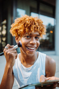 Positive multiracial charismatic boy preparing makeup at his face with visage brush