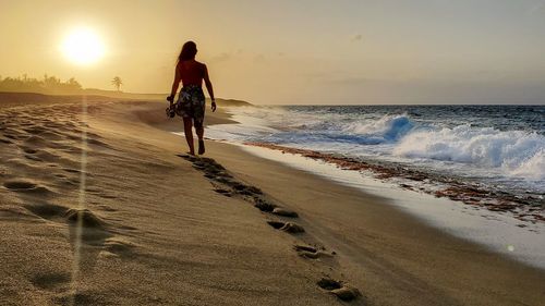 Rear view of woman on beach against sky during sunset