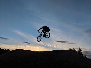 Low angle view of silhouette man performing stunt on bicycle against sky