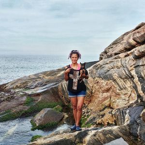 Portrait of young woman standing on rock by sea