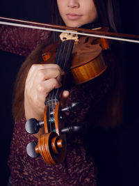 Young woman playing violin against black background