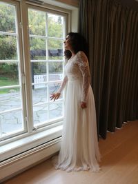 Side view of woman standing by window at home 