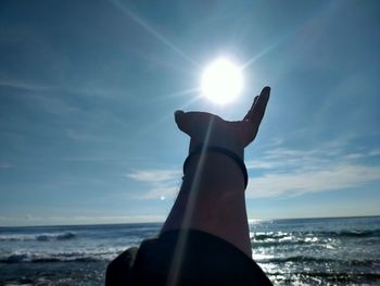 Human hand on sea shore against sky